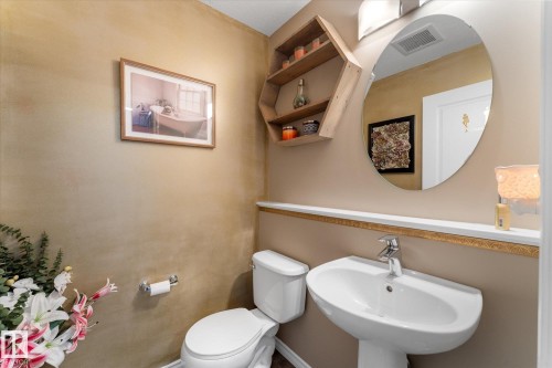 Pedestal sink with chrome faucet, complemented by an oval mirror and a natural wood-finish display shelf - 21818 99A Avenue, Edmonton, AB - Indoor Photo Showing Bathroom
