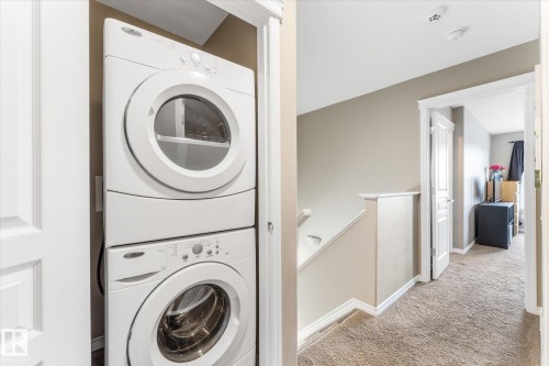 Dedicated laundry closet featuring a white stacked washer and dryer unit, white bi-fold doors, and neutral wall paint - 21818 99A Avenue, Edmonton, AB - Indoor Photo Showing Laundry Room