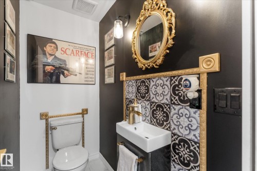Compact powder room featuring a wall-mounted sink with gold-tone faucet, decorative tile backsplash with gold-tone trim, and white toilet - 21818 99A Avenue, Edmonton, AB - Indoor