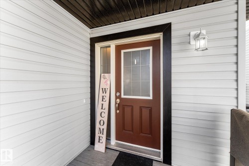 Front entry featuring a brown paneled door with frosted glass, black trim, and a white wall-mounted light fixture - 21818 99A Avenue, Edmonton, AB - Outdoor With Exterior