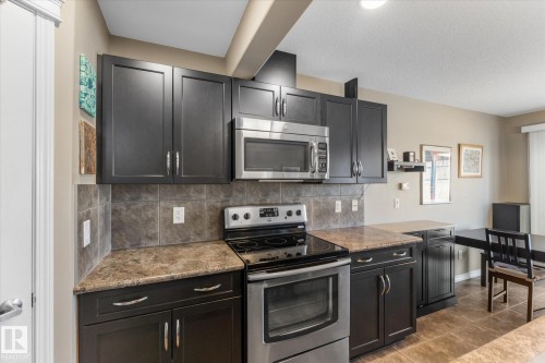 Kitchen featuring dark cabinetry, stainless steel appliances, stone-look countertops, a tiled backsplash, and tiled flooring - 21818 99A Avenue, Edmonton, AB - Indoor Photo Showing Kitchen With Upgraded Kitchen