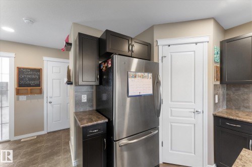 Kitchen featuring dark cabinetry, stainless steel refrigerator, and a light-colored tile backsplash - 21818 99A Avenue, Edmonton, AB - Indoor Photo Showing Kitchen