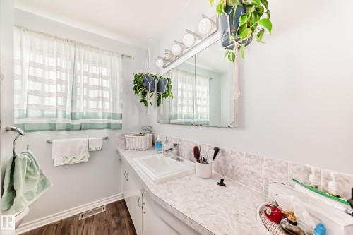 Bathroom featuring a vanity with an integrated sink, a wall-mounted mirror, overhead vanity lighting, and wood-finish flooring - 3611 108 Street, Edmonton, AB - Indoor Photo Showing Bathroom