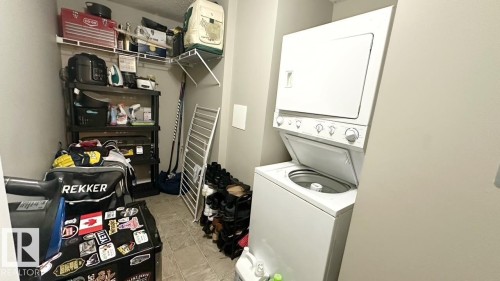 This utility area features a white stacked washer and dryer unit, tiled flooring, and ample shelving for storage - 1112 9363 Simpson Drive, Edmonton, AB - Indoor Photo Showing Laundry Room