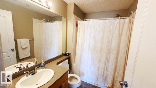 This bathroom features a vanity with an integrated sink, a large mirror, and a shower with a curtain - 1112 9363 Simpson Drive, Edmonton, AB - Indoor Photo Showing Bathroom