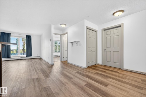 Expansive room featuring wood-finish flooring, white walls, and a large window with white lattice detailing - 215 2208 44 Avenue, Edmonton, AB - Indoor Photo Showing Other Room