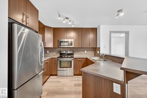 Modern kitchen featuring stainless steel appliances, wood-finish cabinetry, and a breakfast bar - 215 2208 44 Avenue, Edmonton, AB - Indoor Photo Showing Kitchen With Double Sink