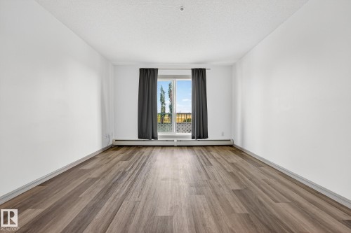 Spacious room featuring wood-finish flooring, white walls, and a large sliding glass door - 215 2208 44 Avenue, Edmonton, AB - Indoor Photo Showing Other Room