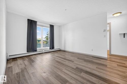 Spacious room featuring wood-finish flooring, white walls, and a large window with a patio access - 215 2208 44 Avenue, Edmonton, AB - Indoor Photo Showing Other Room