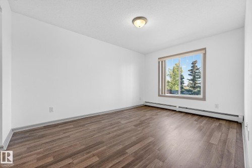 Bright room featuring wood-finish flooring, white walls, and a large window with white blinds - 215 2208 44 Avenue, Edmonton, AB - Indoor Photo Showing Other Room