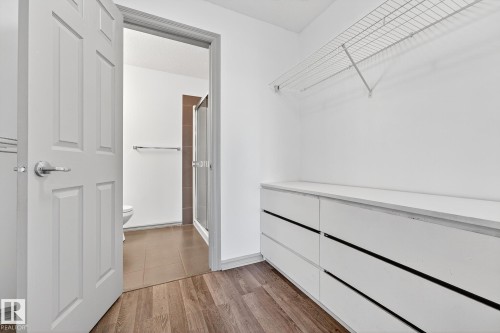 Walk-in closet featuring wood-finish flooring, built-in white dresser cabinetry, and a wire shelving system - 215 2208 44 Avenue, Edmonton, AB - Indoor