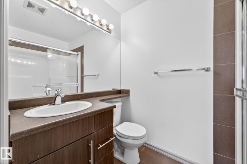 Bathroom featuring a wood-finish vanity with an integrated sink and chrome faucet, a large vanity mirror, and an adjacent toilet - 215 2208 44 Avenue, Edmonton, AB - Indoor Photo Showing Bathroom