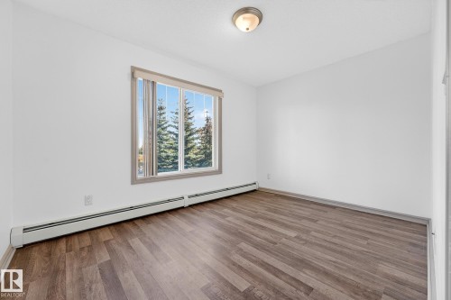 Bright room featuring wood-finish flooring, white painted walls, and a large window with vertical blinds - 215 2208 44 Avenue, Edmonton, AB - Indoor Photo Showing Other Room