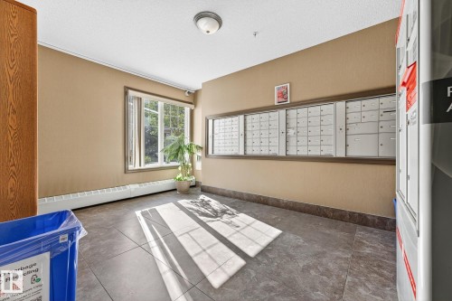 Mailroom area featuring a bank of individual mailboxes, a large window, tiled flooring, and baseboard heating - 215 2208 44 Avenue, Edmonton, AB - Indoor Photo Showing Other Room