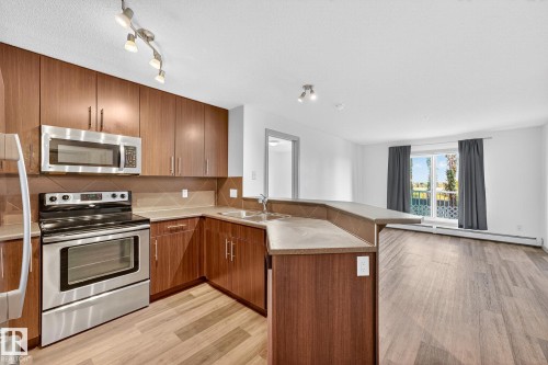 Kitchen featuring stainless steel appliances, wood-finish cabinetry, a neutral-toned backsplash, and a breakfast bar - 215 2208 44 Avenue, Edmonton, AB - Indoor Photo Showing Kitchen With Double Sink