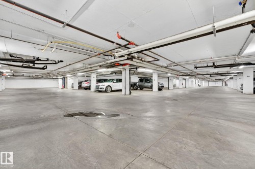 Spacious underground parking facility featuring concrete flooring, exposed ceiling pipes, and overhead fluorescent lighting - 215 2208 44 Avenue, Edmonton, AB - Indoor Photo Showing Garage