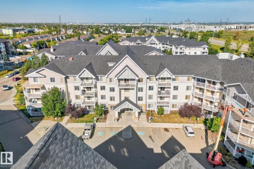 Multi-story residential building featuring light-colored siding, dark shingle roofing, multiple private balconies, and a central entrance with covered portico - 215 2208 44 Avenue, Edmonton, AB - Outdoor With Facade