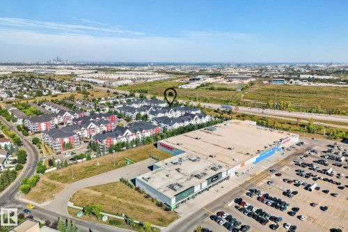 Aerial perspective showcasing a residential development with red and white exterior buildings, adjacent to a large commercial retail center with ample parking - 215 2208 44 Avenue, Edmonton, AB - Outdoor With View