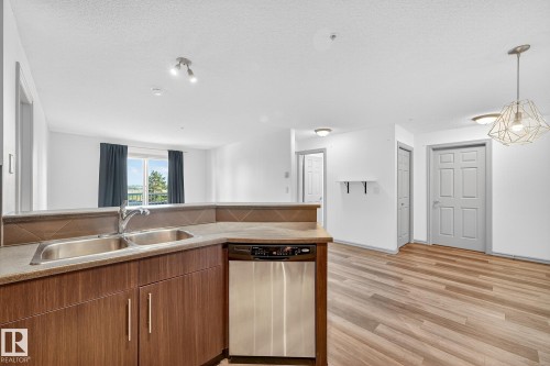 Kitchen featuring wood-finish cabinetry, a stainless steel double sink, and a built-in dishwasher - 215 2208 44 Avenue, Edmonton, AB - Indoor Photo Showing Kitchen With Double Sink