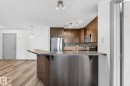 Open-concept kitchen featuring wood-finish flooring, dark wood cabinetry, stainless steel appliances, and a breakfast bar with a stone-finish countertop - 215 2208 44 Avenue, Edmonton, AB  - Indoor Photo Showing Kitchen 