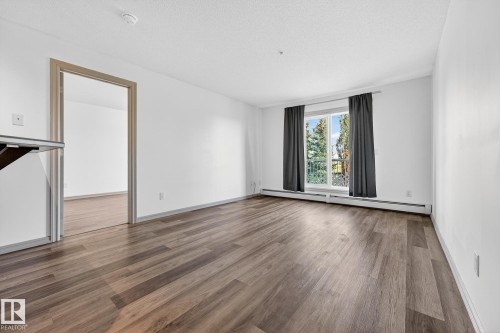 Spacious room featuring wood-finish flooring, crisp white walls, and a large window - 215 2208 44 Avenue, Edmonton, AB - Indoor Photo Showing Other Room
