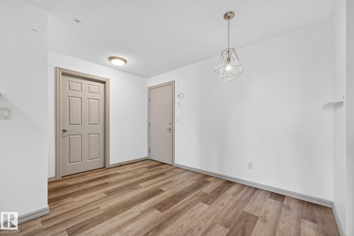 Spacious room featuring wood-finish flooring, neutral paint, a modern geometric pendant light, and a flush-mount ceiling light - 215 2208 44 Avenue, Edmonton, AB - Indoor Photo Showing Other Room