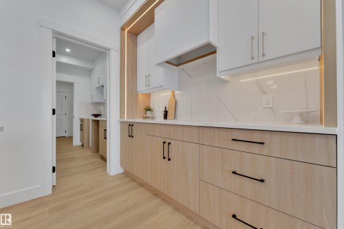 Kitchen featuring two-tone cabinetry with light wood-finish lower cabinets and white upper cabinets, quartz countertops, a matching quartz backsplash, and under-cabinet lighting - 382 Linden Loop, Leduc, AB - Indoor