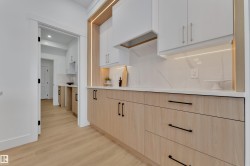 Kitchen featuring two-tone cabinetry with light wood-finish lower cabinets and white upper cabinets, quartz countertops, a matching quartz backsplash, and under-cabinet lighting - 