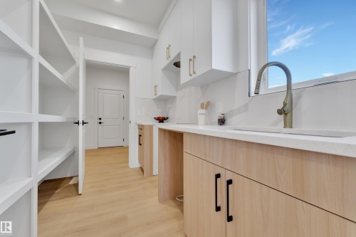 Well-appointed kitchen featuring a window-positioned sink, light-toned wood-finish cabinetry, white upper cabinets, white quartz countertops, and a full-height pantry with shelving - 382 Linden Loop, Leduc, AB - Indoor