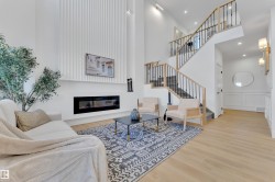 Two-story living area featuring a prominent linear fireplace, vertical wall paneling, light wood-finish flooring, and a multi-level staircase with open risers and wrought iron balusters - 