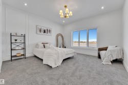 Spacious room featuring light gray carpeting, recessed ceiling lighting, a gold-toned chandelier, large window, and decorative wall molding - 