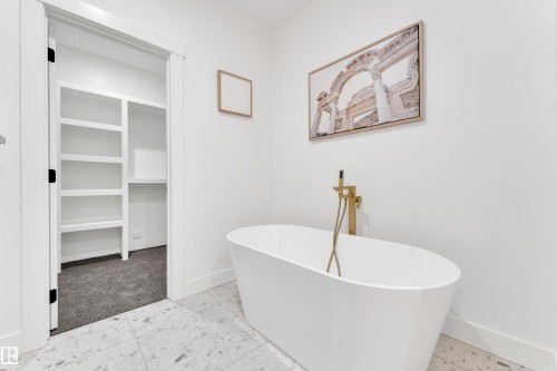 Freestanding soaking tub with a floor-mounted gold-tone faucet, set on light-toned tile flooring - 382 Linden Loop, Leduc, AB - Indoor Photo Showing Bathroom