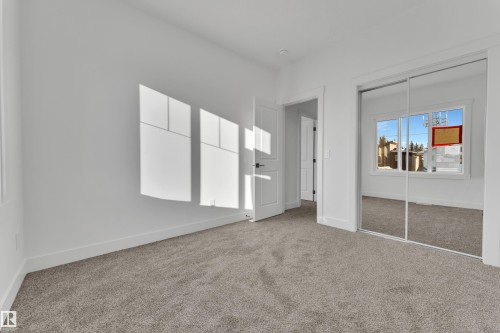 Room featuring neutral carpeting, white walls, white baseboards, a white interior door with dark hardware, and a mirrored closet with sliding doors - 382 Linden Loop, Leduc, AB - Indoor Photo Showing Other Room