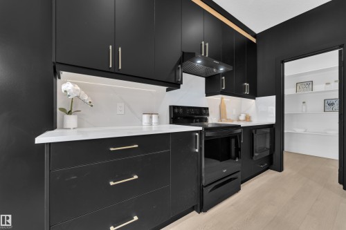Kitchen featuring black cabinetry, light wood-finish flooring, white countertops, built-in appliances, and an adjacent pantry - 259 Linden Loop, Leduc, AB - Indoor Photo Showing Kitchen