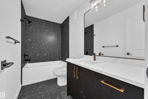 Bathroom featuring a freestanding tub, dark speckled tile surround, matte black fixtures, a contemporary vanity with a white countertop, and gold-finish hardware - 259 Linden Loop, Leduc, AB - Indoor Photo Showing Bathroom