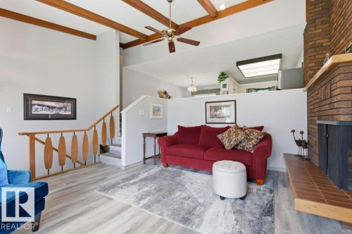 Living area featuring a brick fireplace, wood-finish flooring, vaulted ceilings with exposed wood beams, and a ceiling fan - 8608 22 Ave, Edmonton, AB - Indoor Photo Showing Living Room