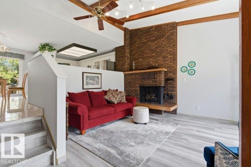 Living area featuring a brick fireplace with a wood mantle, wood-finish flooring, exposed wood ceiling beams, and a ceiling fan with integrated lighting - 8608 22 Ave, Edmonton, AB - Indoor With Fireplace