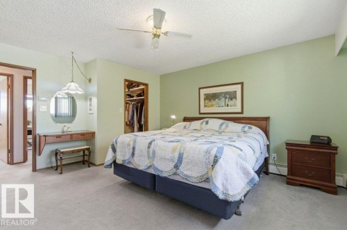 Carpeted bedroom featuring a ceiling fan, a built-in closet with shelving, and a vanity area with a wall-mounted mirror - 8608 22 Ave, Edmonton, AB - Indoor Photo Showing Bedroom