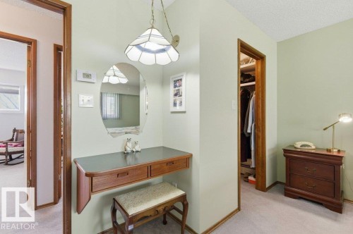 Hallway featuring a built-in vanity with an oval mirror, overhead stained-glass pendant light, and plush wall-to-wall carpeting - 8608 22 Ave, Edmonton, AB - Indoor