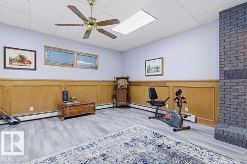 Spacious room featuring wood-finish flooring, half-wall wood paneling, and a drop ceiling with recessed lighting - 8608 22 Ave, Edmonton, AB - Indoor
