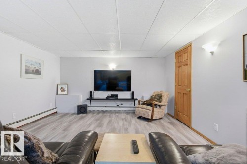 Finished lower-level space featuring wood-finish flooring, white walls, and a drop ceiling - 8608 22 Ave, Edmonton, AB - Indoor Photo Showing Living Room