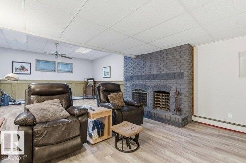 Expansive living area featuring a gray brick fireplace with integrated wine storage, wood-finish flooring, drop ceiling, and wainscoting - 8608 22 Ave, Edmonton, AB - Indoor With Fireplace