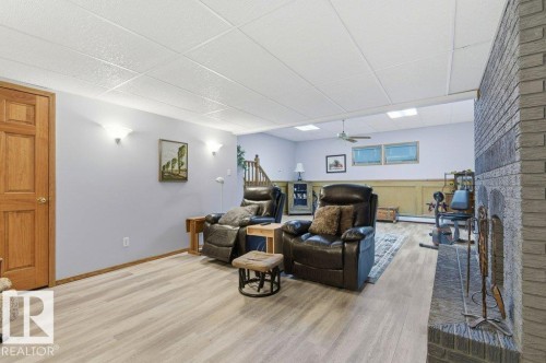 Spacious lower-level area featuring light wood-finish flooring, a stone-clad fireplace, and a drop ceiling with recessed lighting - 8608 22 Ave, Edmonton, AB - Indoor