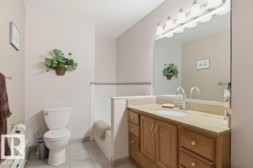 Bathroom featuring a wood-finish vanity with a granite-style countertop and an integrated sink, a large wall-mounted mirror, and a five-light vanity fixture - 8608 22 Ave, Edmonton, AB - Indoor Photo Showing Bathroom