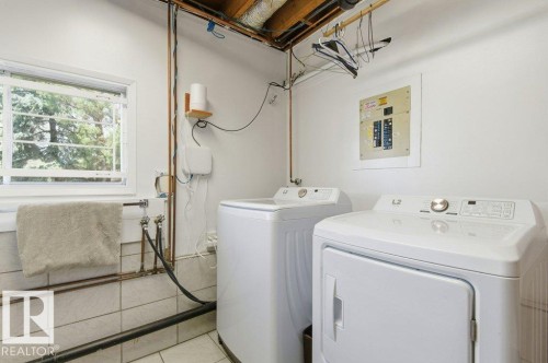 Dedicated laundry area featuring a window, tiled lower wall, exposed ceiling joists, and a visible electrical panel - 8608 22 Ave, Edmonton, AB - Indoor Photo Showing Laundry Room