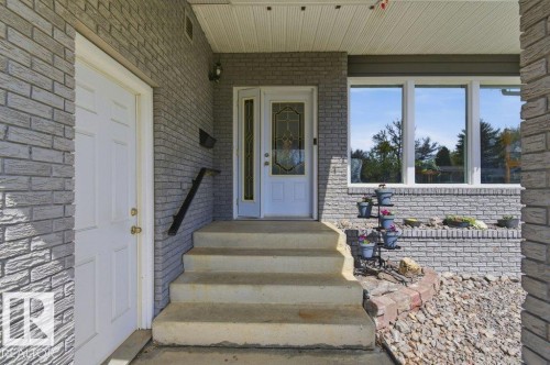 Front entrance with gray brick facade, white entry door with decorative glass, concrete steps, and a black handrail - 8608 22 Ave, Edmonton, AB - Outdoor With Exterior