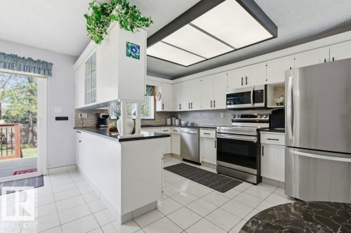 Kitchen featuring white cabinetry, dark countertops, and stainless steel appliances including a refrigerator, range, microwave, and dishwasher - 8608 22 Ave, Edmonton, AB - Indoor Photo Showing Kitchen