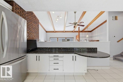 Kitchen counter with white cabinetry, dark stone-finish countertop, and a built-in breakfast bar - 8608 22 Ave, Edmonton, AB - Indoor