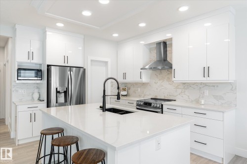 Contemporary kitchen featuring an island with a built-in sink, white cabinetry with black hardware, recessed lighting, and stainless steel appliances - 1214 Eaton Lane, Edmonton, AB - Indoor Photo Showing Kitchen With Double Sink With Upgraded Kitchen