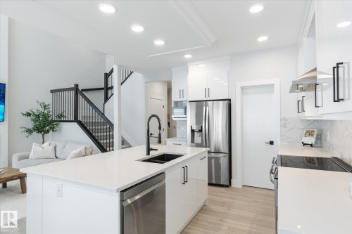 Modern kitchen featuring a large island with an undermount sink, stainless steel appliances, white flat-panel cabinetry, and light wood-finish flooring - 1214 Eaton Lane, Edmonton, AB - Indoor Photo Showing Kitchen With Double Sink With Upgraded Kitchen